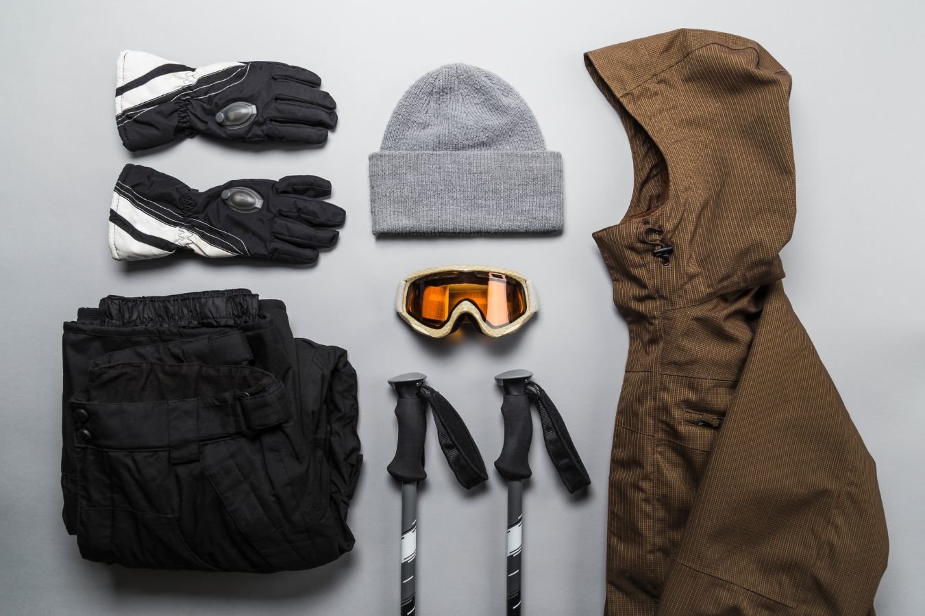 Image of what to wear alpine touring. Clothing shown includes hat, gloves, outer shell (jacket), goggles, ski poles, and snowpants.